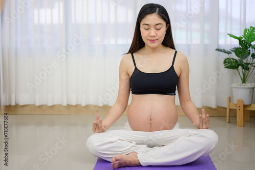 A pregnant woman trains with yoga in her living room at home while awaiting the birth of her baby - Concept of health and wellness