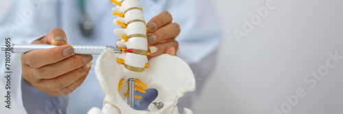 An orthopedic surgeon holds a spinal model as he demonstrates treatment methods for human spinal injuries caused by back pain during a medical consultation. photo
