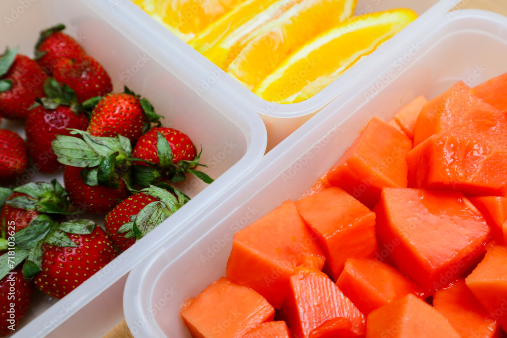 plastic containers containing papaya, strawberries and oranges, on a wooden background plastic containers containing papaya, strawberries and oranges, on a wooden background