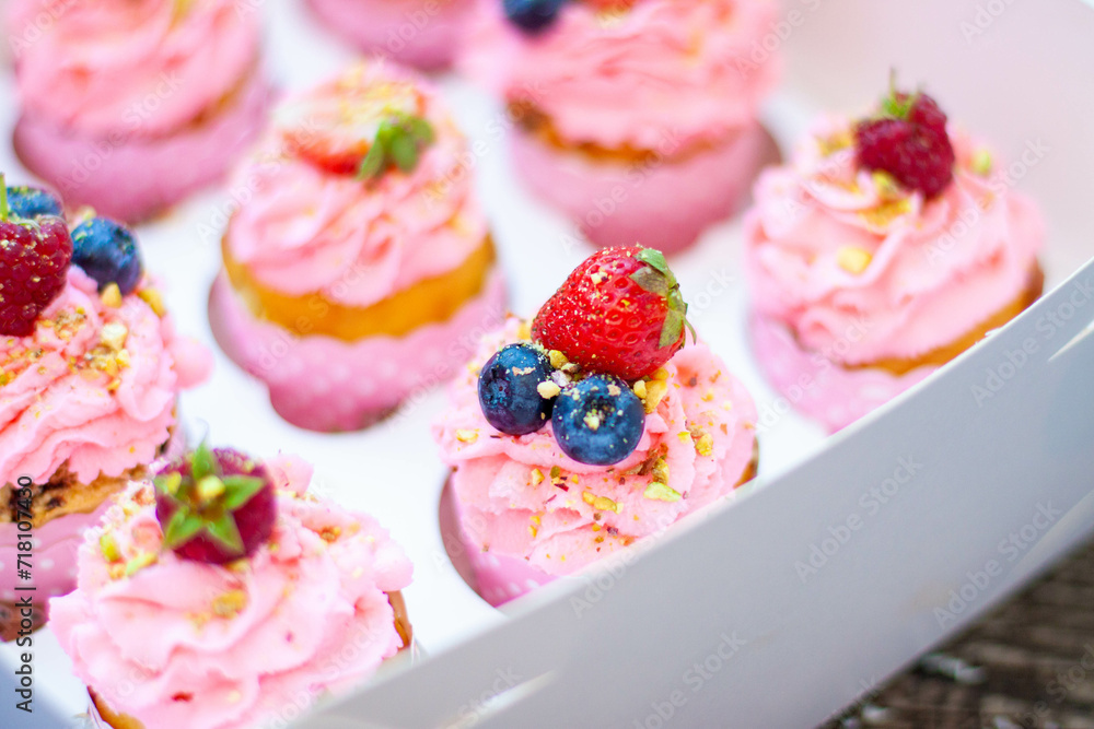 Festive pink cupcakes with fresh strawberries, raspberries and blueberries on cardboard box with chopped pistachios on the top Festive pink cupcakes with fresh strawberries, raspberries and blueberries on cardboard box with chopped pistachios on the top