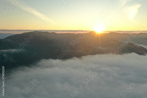 Aerial view of beautiful mountains covered with fluffy clouds at sunrise