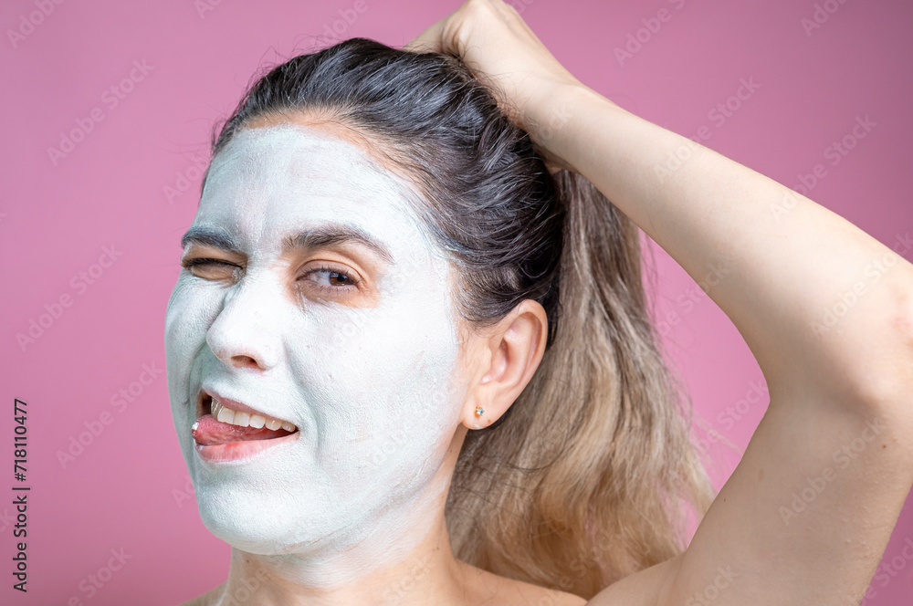 Fototapeta premium Portrait of a woman with a cosmetic mask on her face. A cheerful woman with a white face.