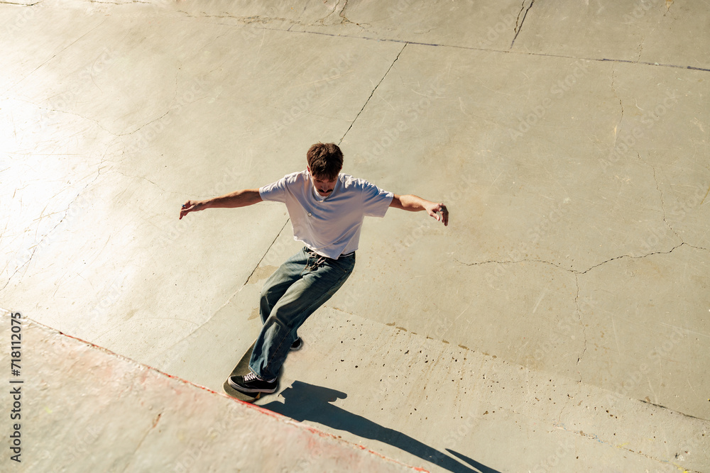 Full body of young male skater in casual outfit doing trick on skateboard riding in skate park