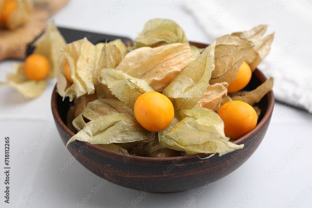 Ripe physalis fruits with calyxes in bowl on white table, closeup Ripe physalis fruits with calyxes in bowl on white table, closeup