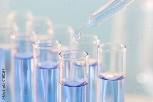 Laboratory analysis. Dripping light blue liquid from pipette into glass test tube on blurred background, closeup