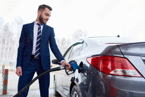 Side view at man wearing suit while refueling gas tank of car in petrol station, copy space © Mediaphotos