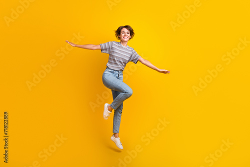 Full length photo of cheerful lovely person jumping arms wings flying empty space isolated on yellow color background