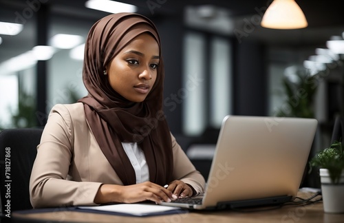 Young muslim woman wearing hijab sitting working with laptop computer in her modern business office
