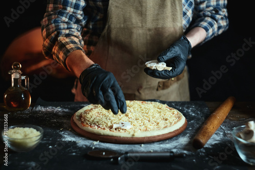 Pizzaiola cooking pizza in the oven. Chef in a leather apron puts mushrooms on pizza.
