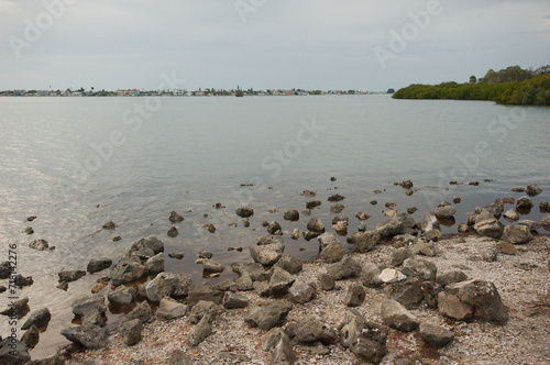 View over rocks in foreground and bay water looking south west from Turtle Crawl Point at War Veterans Memorial Park in St.Petersburg, Florida. Green trees on the side. Near sunset on a cloudy day.   © Del Harper