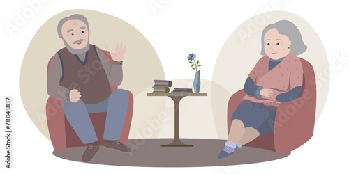 Couple of pensioners sitting in armchairs opposite each other. Man is speaking, woman is listening. Coffee table with books and vase with flower is between armchairs.