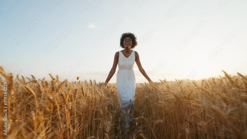 Travel concept. Graceful black woman afro hair runs in white dress across field of golden wheat towards wind smiling rejoices on walk in summer at sunset blue sky slow motion. Go Everywhere. Freedom Travel concept. Graceful black woman afro hair runs in white dress across field of golden wheat towards wind smiling rejoices on walk in summer at sunset blue sky slow motion. Go Everywhere. Freedom