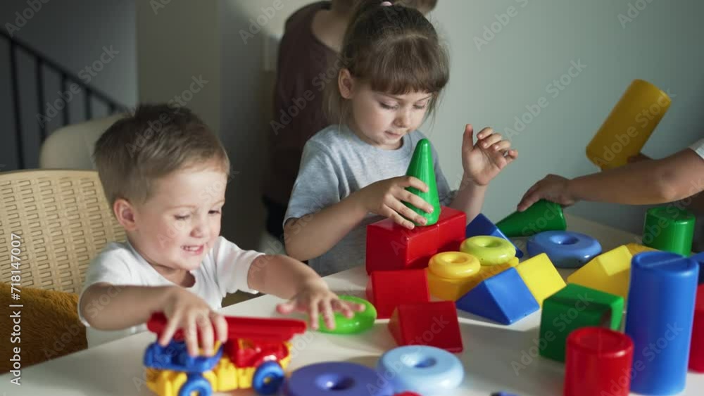 Happy family. Puzzle game. Colored toy in the hands of children. Teaching children in kindergarten. Boys and girls teamwork build cubes. Colored blocks and toy car on table in kindergarten. Schooling Happy family. Puzzle game. Colored toy in the hands of children. Teaching children in kindergarten. Boys and girls teamwork build cubes. Colored blocks and toy car on table in kindergarten. Schooling