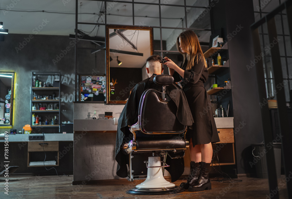 Beautiful Young female barber making men's hairstyle using Haircut Clipper in Modern loft style barber shop interior. Haircare services local small businesses, cosmetics and personal care industry.