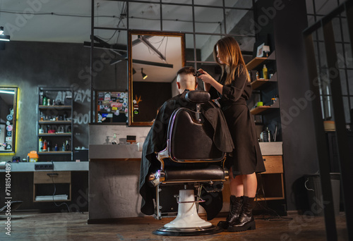 Beautiful Young female barber making men's hairstyle using Haircut Clipper in Modern loft style barber shop interior. Haircare services local small businesses, cosmetics and personal care industry.