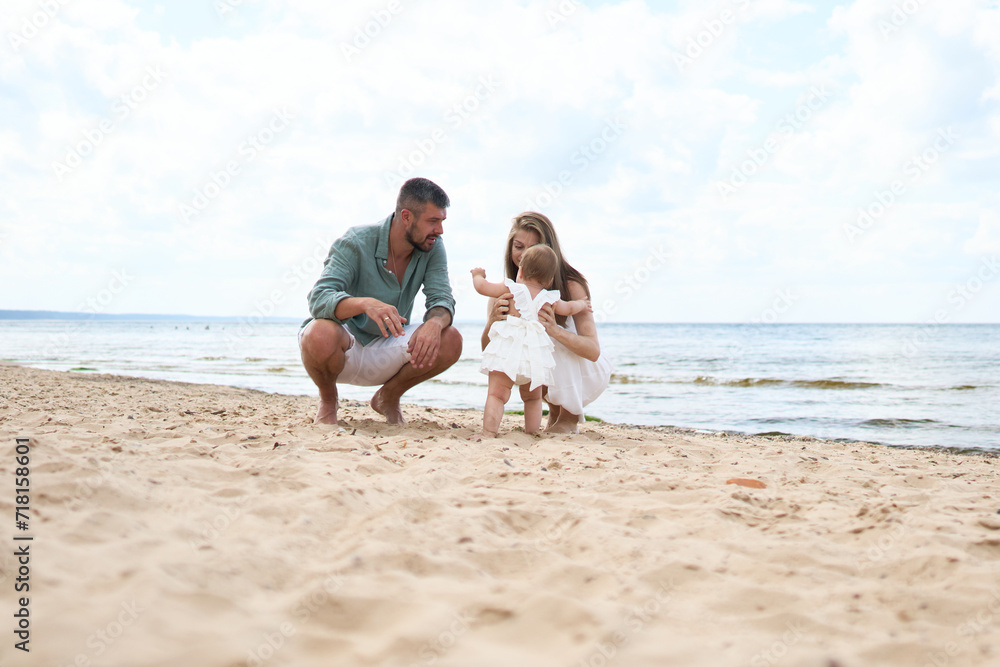 A photoshoot of happy parents playing with their 1 year old girl playing on sand near the beach
