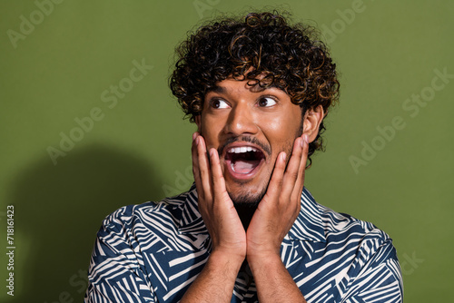 Portrait of funky young funny guy touching cheeks looking left side empty space impressed reaction isolated on khaki color background