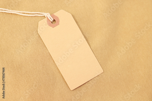 Cardboard tag on beige garment, top view. Space for text