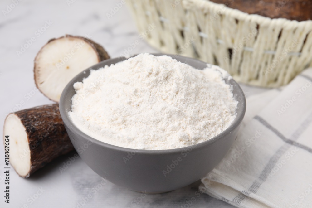 Bowl with cassava flour and roots on white marble table, closeup Bowl with cassava flour and roots on white marble table, closeup