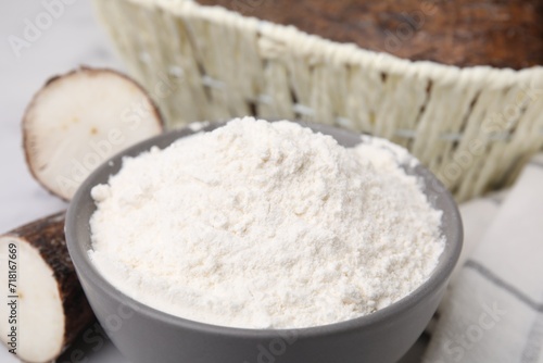 Bowl with cassava flour and roots on table, closeup