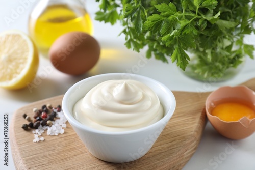 Tasty mayonnaise sauce in bowl, spices and ingredients on white table, closeup
