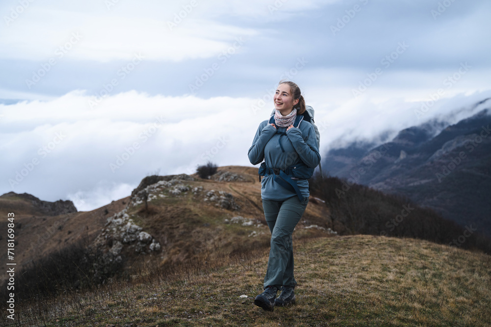 A young girl mountaineer walks and laughs in hiking clothes on the top of a mountain above the clouds, hiker having trekking day out on a windy day, sport and inspirational concept A young girl mountaineer walks and laughs in hiking clothes on the top of a mountain above the clouds, hiker having trekking day out on a windy day, sport and inspirational concept