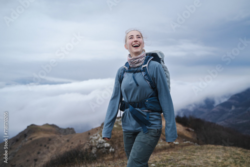 Smiling, portrait of a happy young girl with straight brown hair in a ponytail and wearing hiking clothes on a mountain top above the clouds, woman enjoying the view