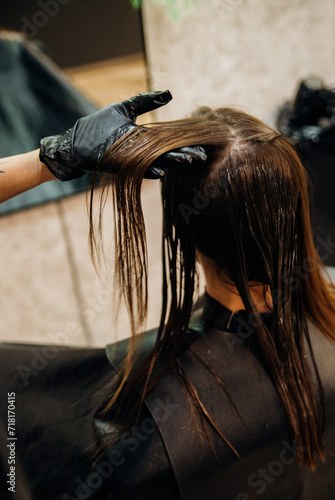 Close-up of a woman's head in the process of hair coloring in a beauty salon. Close-up of a woman's hands in black gloves coloring her hair with a brush. Kerating of hair.