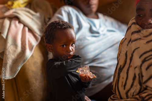village african boy eating a snack in the room together with his mom and granny photo