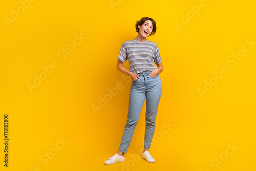 Full length photo of cheerful adorable girl dressed stylish clothes looking empty space offer poster isolated on yellow color background