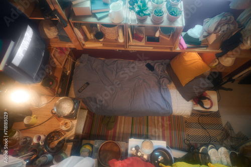 Interior of small apartment or microflat with single bed surrounded by wooden shelves, old TV set, kitchen table and other stuff
