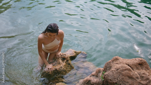 Swimming lady climbing rock deep lake. Young woman sitting brown volcanic stones