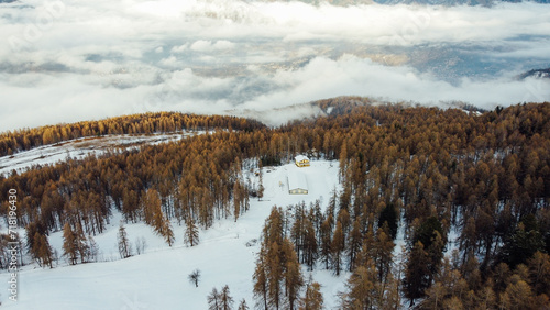 Aerial view of winter landscape with mountain slopes covered with snow, fluffy clouds and coniferous forest. Natural background.