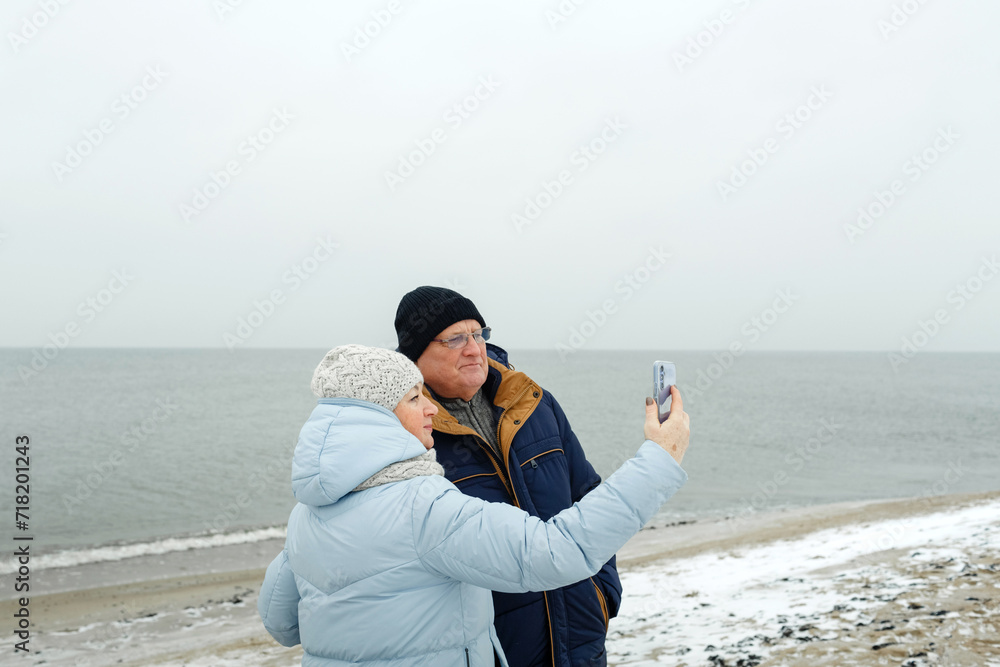 Elderly couple enjoying a winter walk on the beach, taking a selfie. Elderly couple enjoying a winter walk on the beach, taking a selfie.