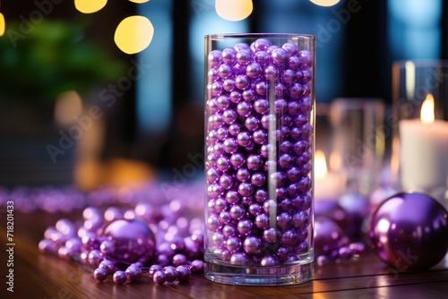  a glass filled with purple balls on top of a wooden table next to a candle and a glass filled with purple balls on top of a wooden table next to a candle.