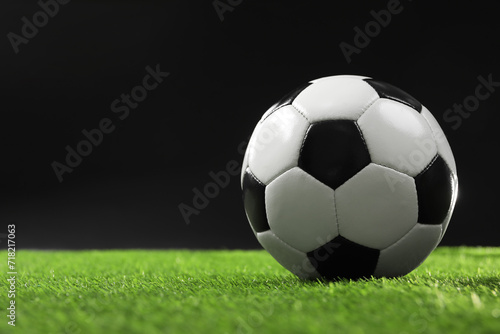 Soccer ball on green grass against black background  space for text