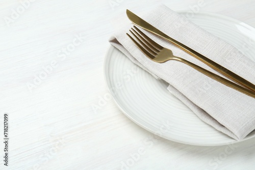 Stylish ceramic plate, cutlery and napkin on white wooden table, closeup. Space for text