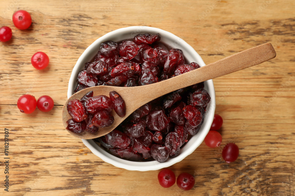 Tasty dried cranberries in bowl and fresh ones on wooden table, top view Tasty dried cranberries in bowl and fresh ones on wooden table, top view