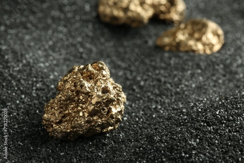 Shiny gold nugget on black sand, closeup. Space for text