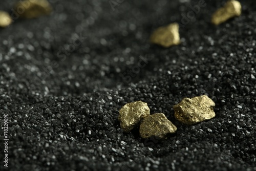Shiny gold nuggets on black sand, closeup. Space for text