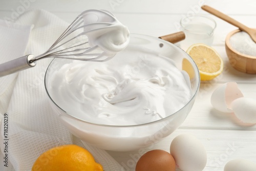 Bowl with whipped cream, whisk and ingredients on white wooden table