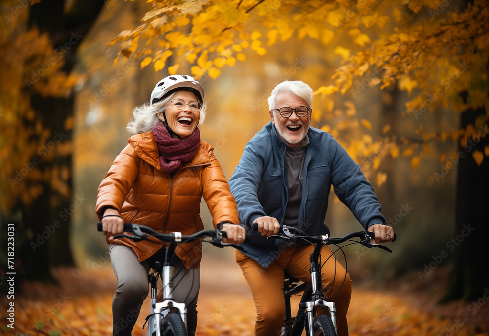 An elderly couple shares laughter while cycling together through a park adorned with fall foliage, exemplifying active senior living