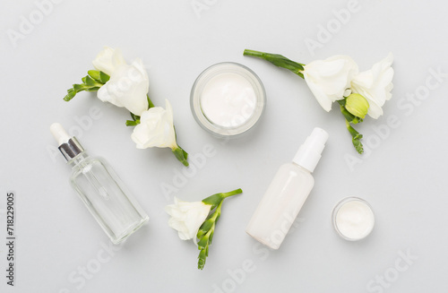 Facial cosmetic products with freesia flowers on color background, top view