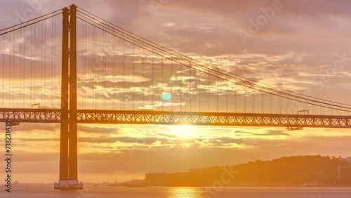 Lisbon city sunrise with April 25 bridge timelapse, River and waterfront early morning. Orange clouds on the sky photo