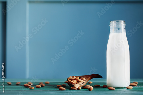 Whole fresh almonds in a wooden spoon with a bottle of fresh creamy almond white milk over a rustic table or background. Selective focus with blurred background.