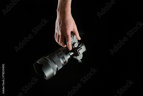 young photographer holding a mirrorless camera in his hand isolated on black background