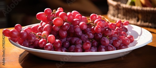 The red grape berries, arranged neatly in a white plate on a delicate straw tray, garnered attention with their vibrant colors in a captivating closeup. photo