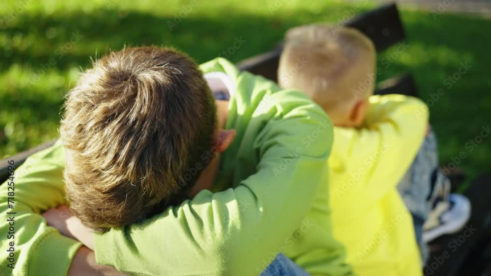 Two young boys in bright green sit back-to-back, sibling quarrel outdoors. No compromising, not talking. Rivalry concept Two young boys in bright green sit back-to-back, sibling quarrel outdoors. No compromising, not talking. Rivalry concept