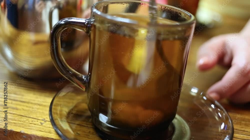 Close up of glass of tea and lemon, in which sugar is mixing with spoon Close up of glass of tea and lemon, in which sugar is mixing with spoon