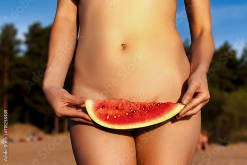 Crop photo of naturist lady posing covering watermelon naked on beach, close up. Perfect nude woman with sexy body, no clothes. Nudism naturism lifestyle concept, clothing optional. Copy ad text space